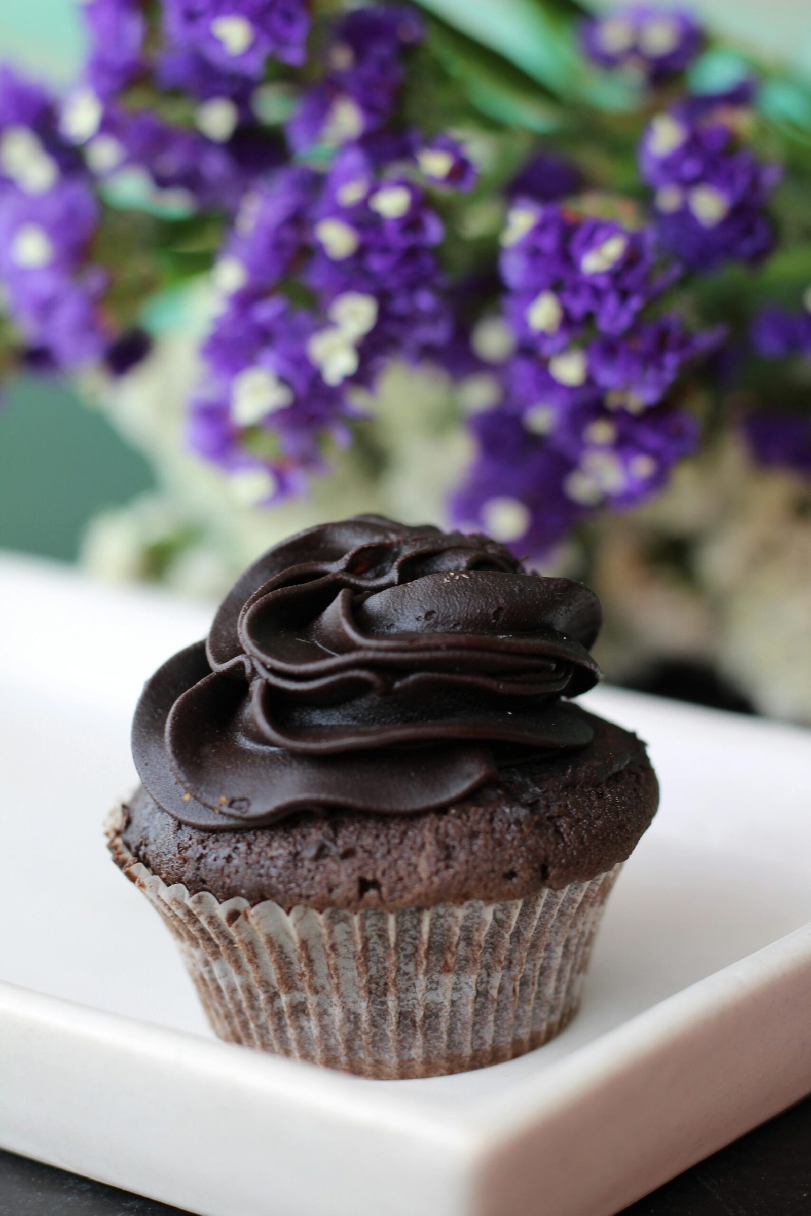 A rich chocolate cupcake topped with creamy icing and a floral backdrop.