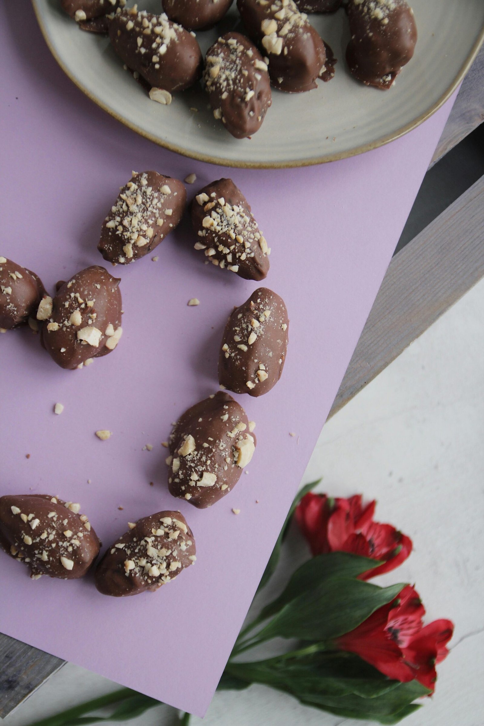 Handmade chocolate-covered dates with nuts and red flowers on pastel background.